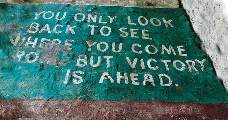 Green paint on the ground with faded white text that reads "You only look back to see where you come from, but victory is ahead."