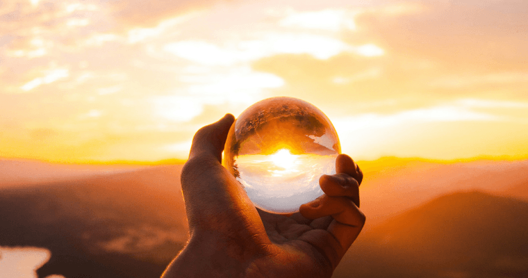 A person holds a clear ball against a golden sun.
