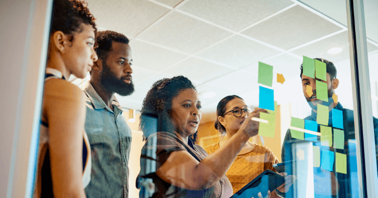 A group of diverse leaders collaborate on a wall with multicolored notes to strategize.