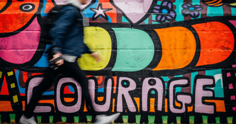 A man walks past a multi-colored wall that says "courage".